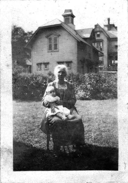 August 1925, notice the cupola on carriage house and the smaller 4 windows on bottom floor. Also, notice on main house, the back porch, one story. Mrs. Gabriel Evans, of 7 Athens street in foreground of picture, holding her granddaughter, Esther Evans.